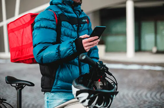 Entregador de aplicativo com jaqueta azul segurando um celular com a mãe direita